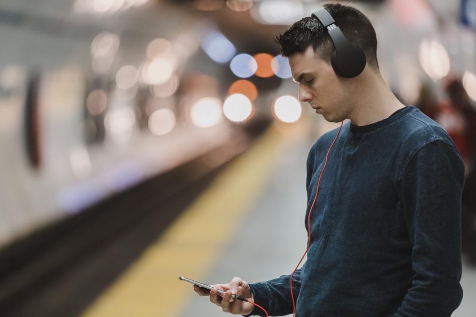 A young man wearing headphones, looking at his phone