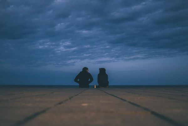 Due persone sedute una accanto all'altra su un molo, con lo sguardo verso il mare