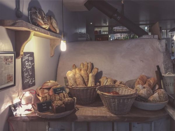 A bakery counter with baskets of fresh bread and rolls under a warm lamp