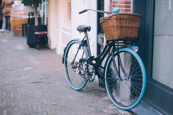 A bicycle with a wicker basket parked against a building on a city street