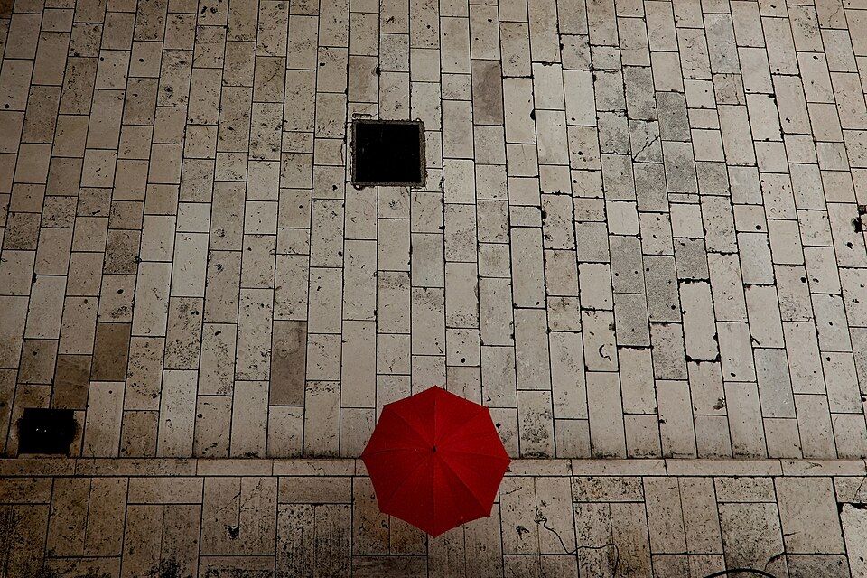 A red umbrella seen from above on a wide stone pavement