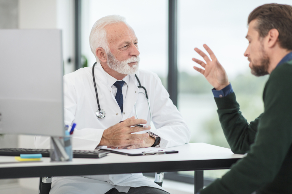 A doctor in a white coat talking with a patient across a desk