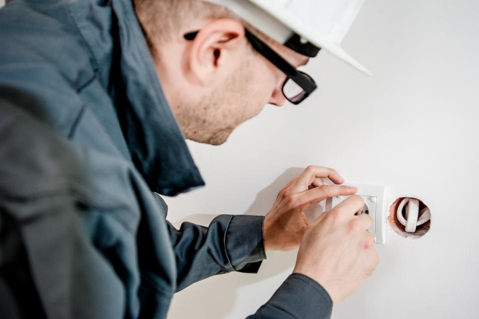 An electrician in a hard hat installing a socket on a white wall