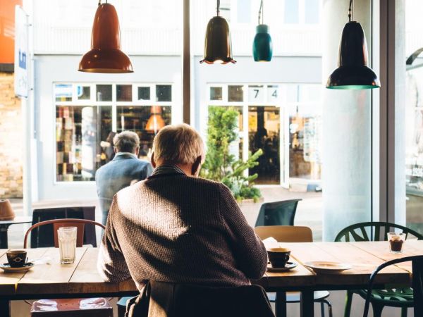 An older man sitting at a café table by a large window