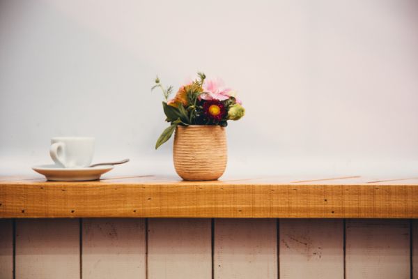 A cup of coffee and a small vase of flowers on a wooden counter