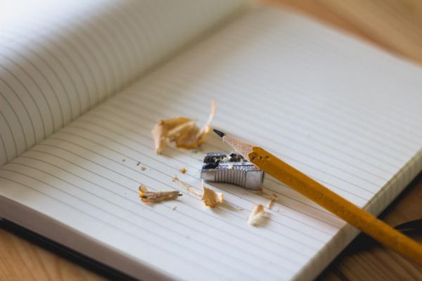 An open lined notebook with a pencil and a pencil sharpener