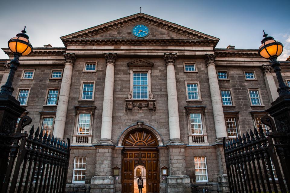 The stone front of a historic university building with lanterns at the gate