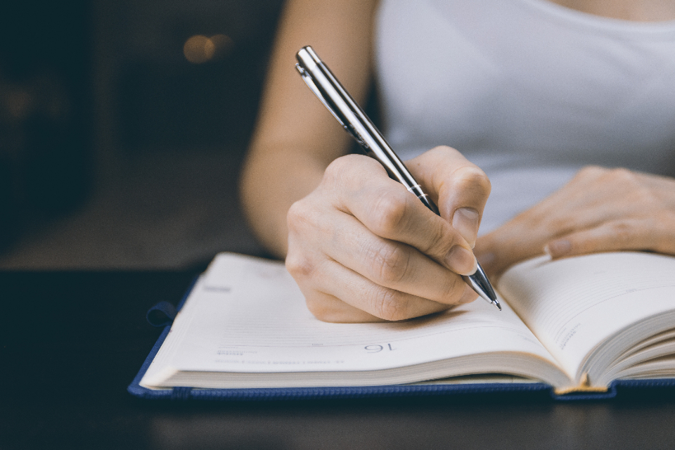 A hand writing with a pen in an open notebook