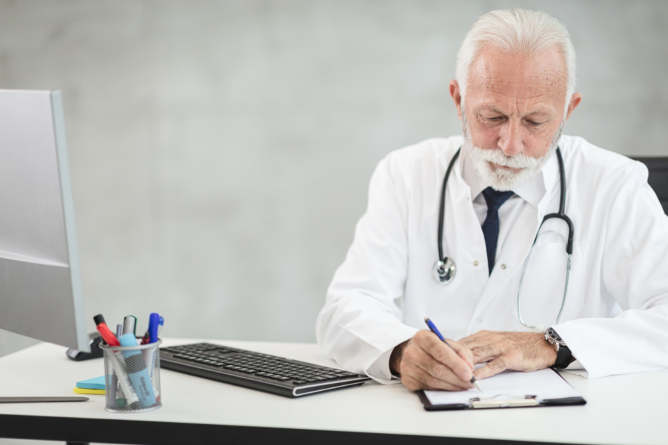 Un médico con bata blanca tomando notas en su escritorio