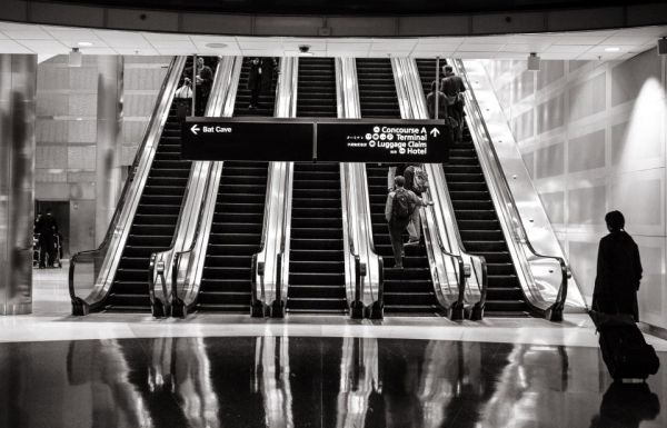 Viajeros en las escaleras mecánicas de un aeropuerto, uno de ellos esperando con su maleta
