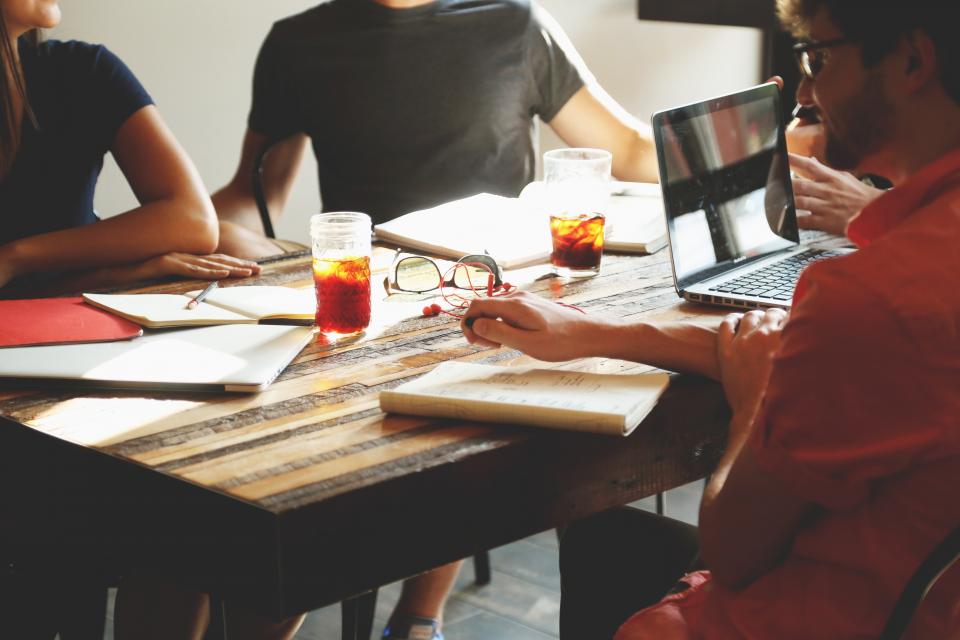 Colleagues around a table with laptops, notebooks and drinks