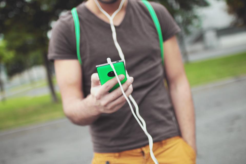 A young man walking outside with earphones and a smartphone in his hand