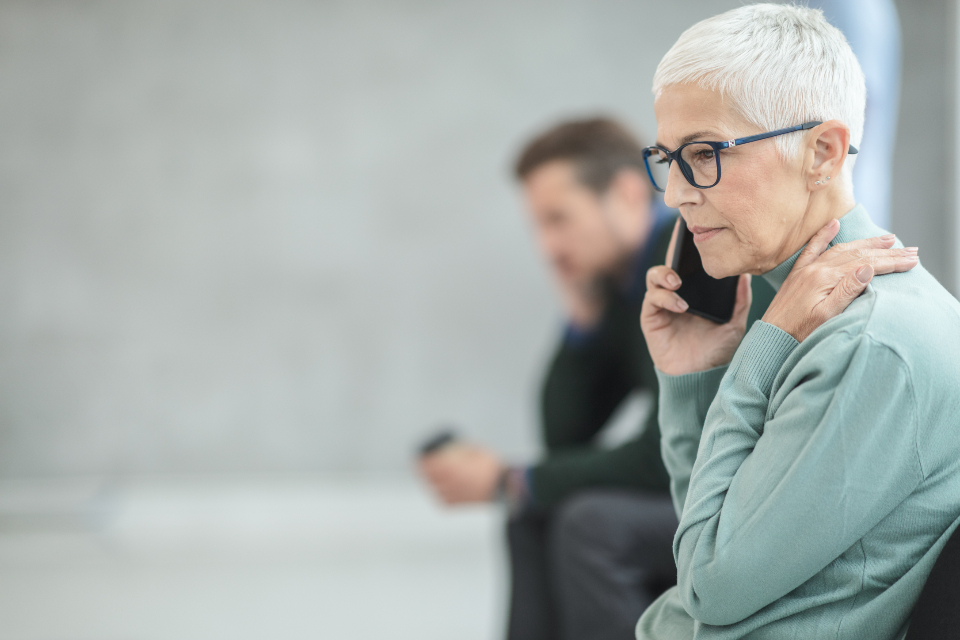 A woman with short grey hair and glasses listening carefully on a phone call