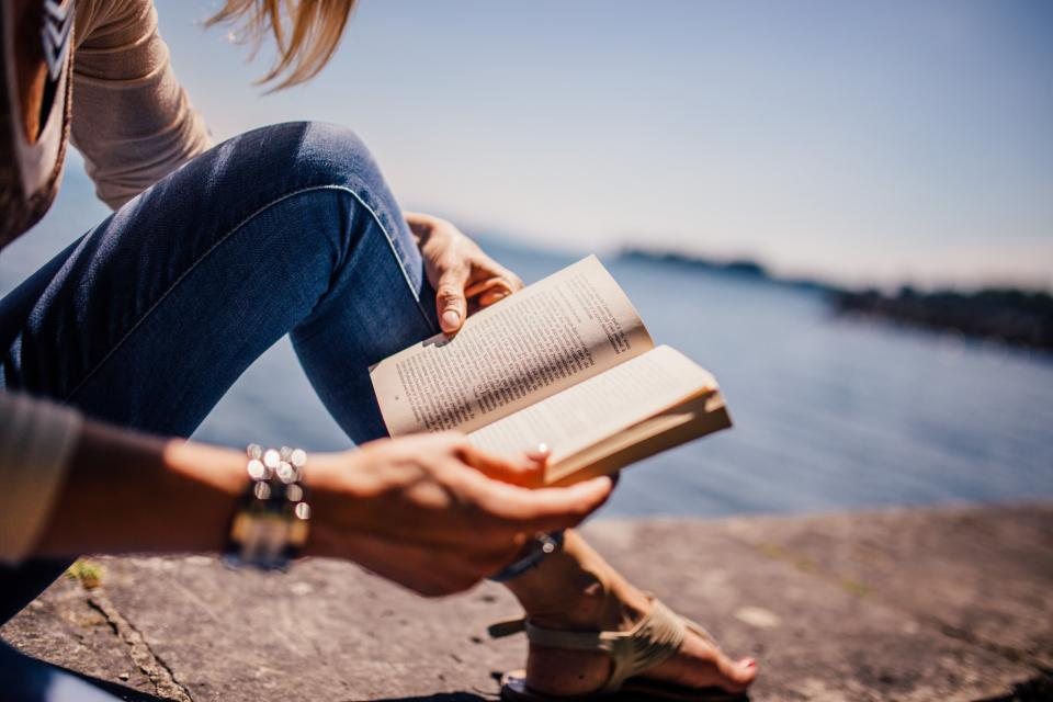 A person reading a book outdoors beside the water