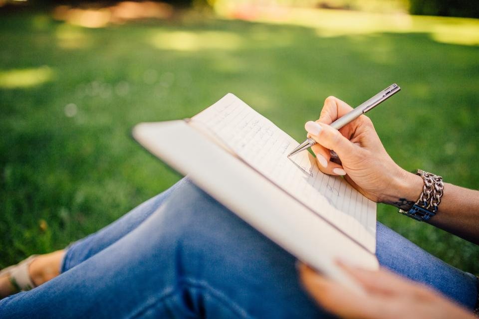 A person writing in a notebook outdoors on the grass