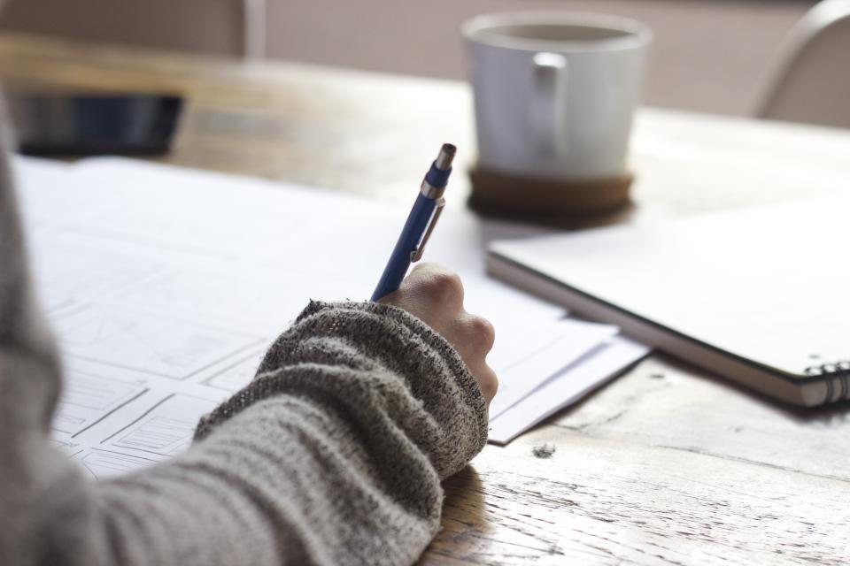 A person writing in a notebook next to a cup of coffee